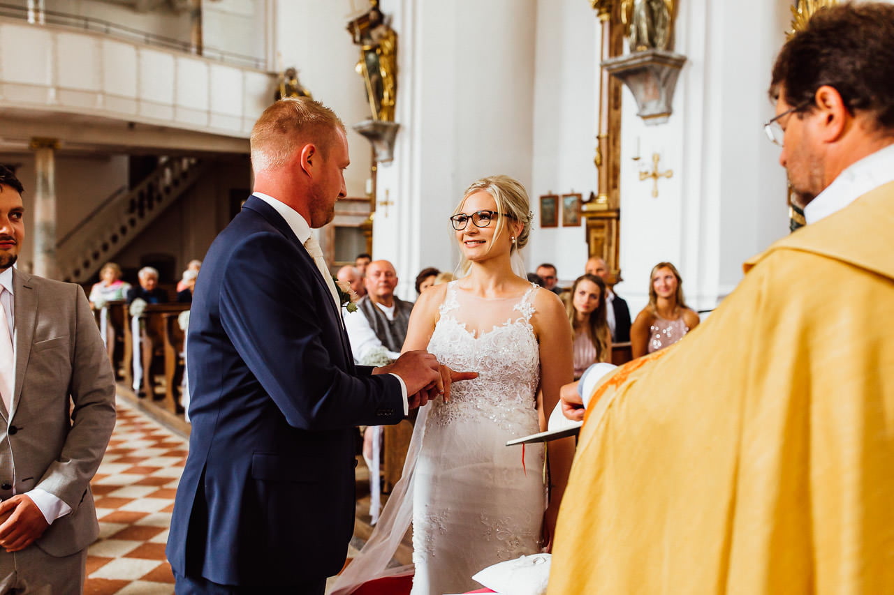 Der Bräutigam steckt der Braut bei einer kirchlichen Trauung in München einen Ring an den Finger