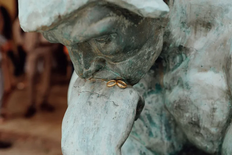Goldene Eheringe auf den Händen einer Gartenskulptur - Symbol der Eiserne Hochzeit.