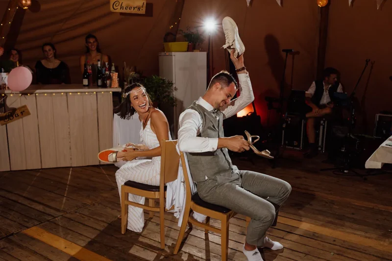 Fröhliches Paar spielt das Hochzeitsspiel 'Schuhe heben' auf ihrer Hochzeit.