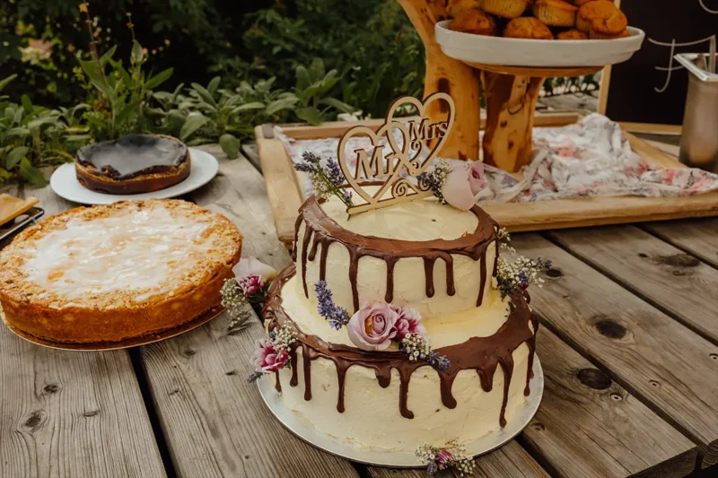 Zweistöckige Hochzeitstorte mit Schokoladenglasur, Rosen und einem Holzschild 'Mr&Mrs' - Alles über Hochzeitstorte Preise und Gestaltungsmöglichkeiten.