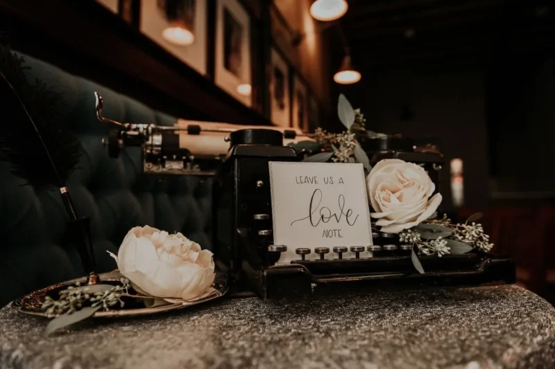 Romantische Elfenbeinhochzeit: Liebevolle Details mit einer Maschine zum Schreiben, einer Karte mit dem Aufdruck 'Liebe' und zarten weißen Blüten.