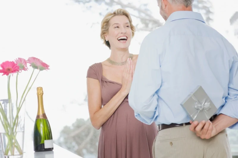 Ein Mann, der hinter seinem Rücken ein Geschenk für seine Frau versteckt, um den 33. Hochzeitstag, die Zinnhochzeit, zu feiern.