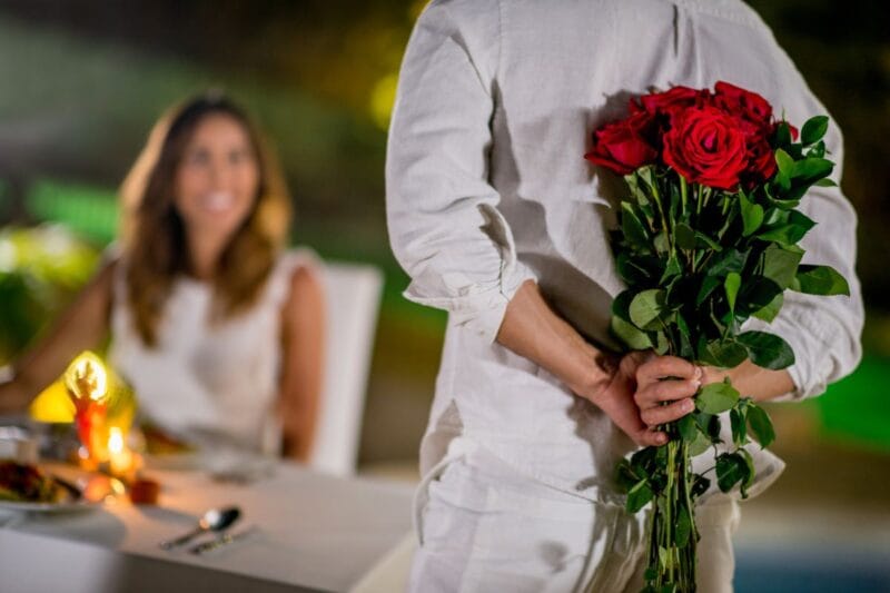 Ein Mann hält einen Strauß roter Rosen hinter seinem Rücken, um ihn seiner Frau zum Seidenhochzeitstag zu schenken.