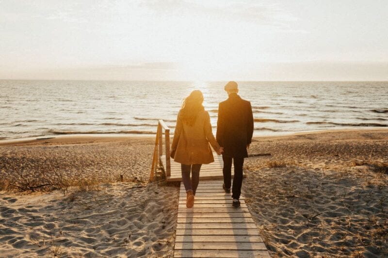 Ein verliebtes Paar spaziert am Strand entlang und betrachtet den Sonnenuntergang, während sie sich fragen, Wann heiraten.