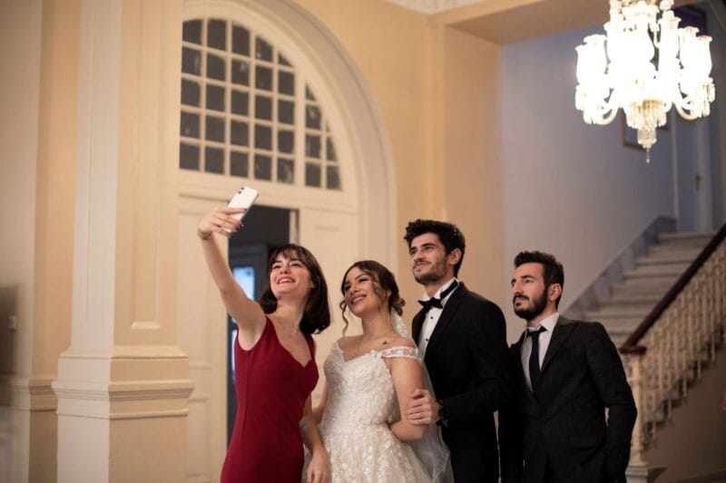 Ein frisch vermähltes Paar macht gemeinsam mit den Hochzeitsgästen ein Selfie, was als moderne Interpretation von Hochzeitsbräuche betrachtet werden kann.