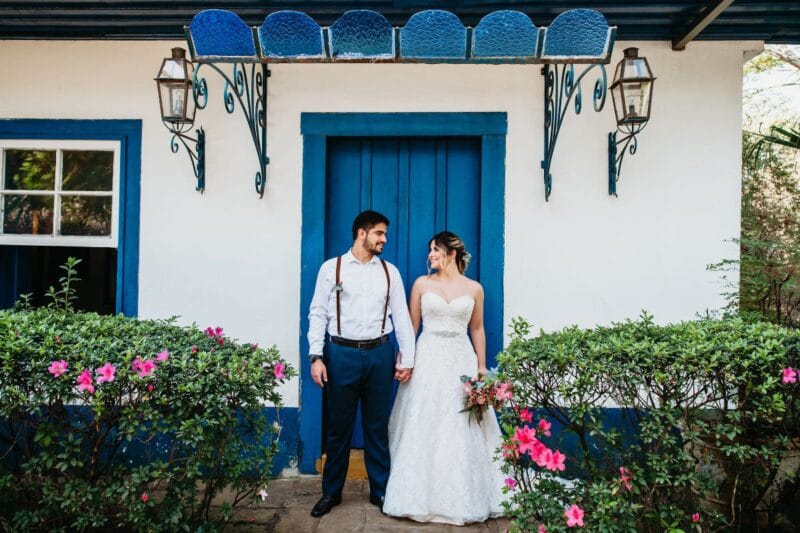 Ein glückliches Paar feiert eine Low-Budget-Hochzeit vor einem charmanten Haus mit blauen Türen.