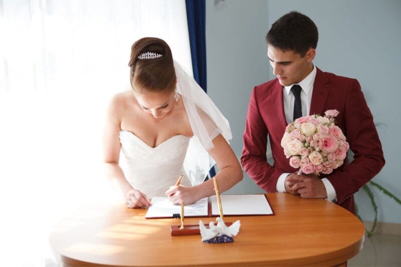 Eine glückliche Braut und Bräutigam, die gemeinsam Dokumente unterzeichnen, um ihre Namensänderung nach der Hochzeit zu bestätigen.
