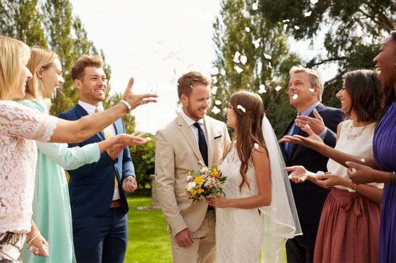 Bild: Glückliches Hochzeitspaar wird von Gästen umgeben, die ein Spalier bilden.