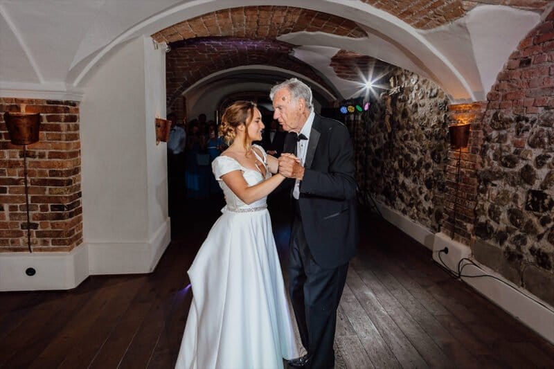 Eine berührende Szene, in der die Braut eng mit ihrem Vater tanzt, während sie strahlend lächelt, um den emotionalen Vater-Tochter-Tanz zu feiern.