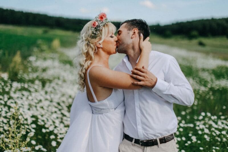 Ein romantisches Bild eines Brautpaares, das sich vor einem Hintergrund aus blühenden Feldblumen küsst, während sie die Frage diskutieren, wer die Hochzeit bezahlt.