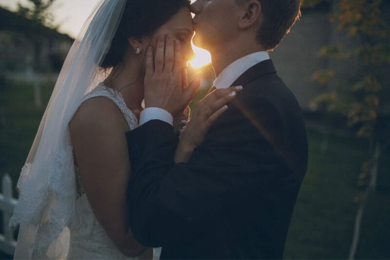 Ein romantisches Bild einer küssenden Braut und eines Bräutigams am Sonnenuntergang, das die Schönheit einer Hochzeit symbolisiert.
