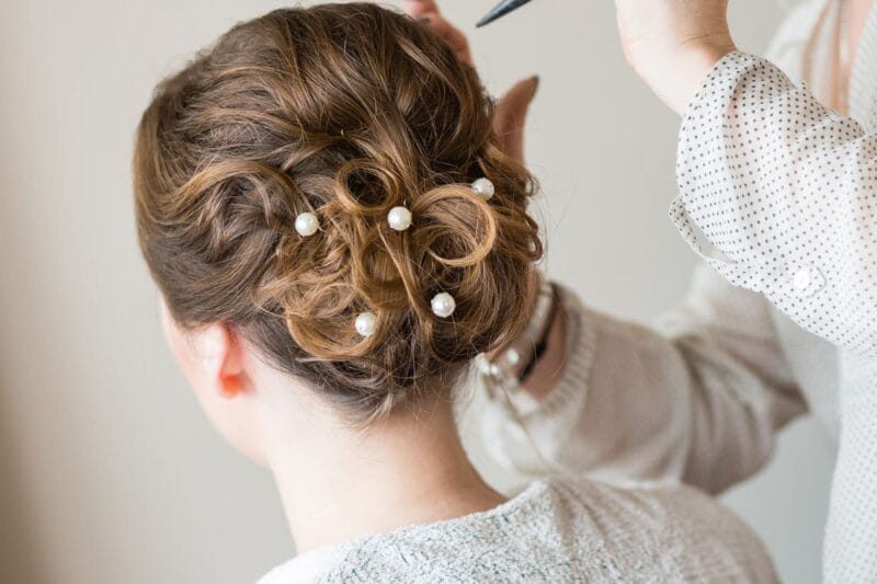 Die Braut wird für ihren großen Tag gestylt, mit einer eleganten Brautfrisur halboffen.