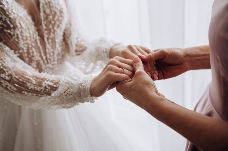 Eine Braut und ihre Mutter halten sich liebevoll an den Händen während der Hochzeitsvorbereitungen.