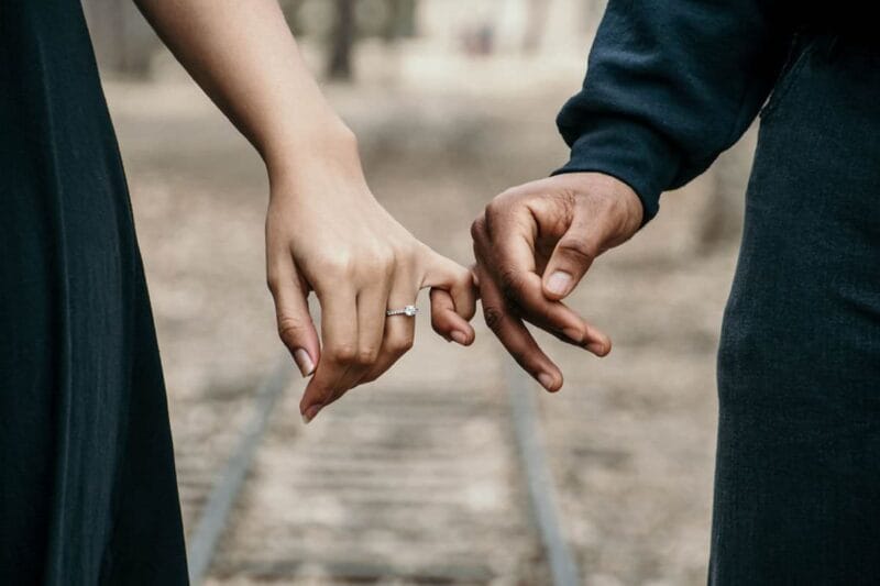Eine männliche und eine weibliche Hand halten sich an den Fingern fest, um ihre Verlobung bekannt geben.