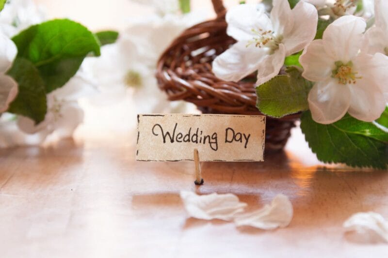 Nahaufnahme eines Notfallkörbchens für die Hochzeit, dekoriert mit weißen Blumen und einem handgeschriebenen Schild "Wedding Day".
