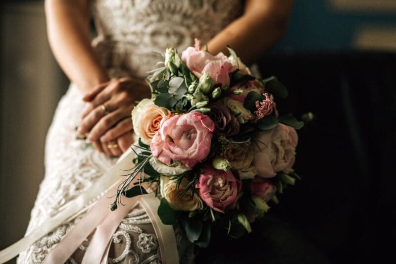 Eine Braut hält ihren Brautstrauß Wasserfall aus verschiedenen Blumenarten in der Hand.