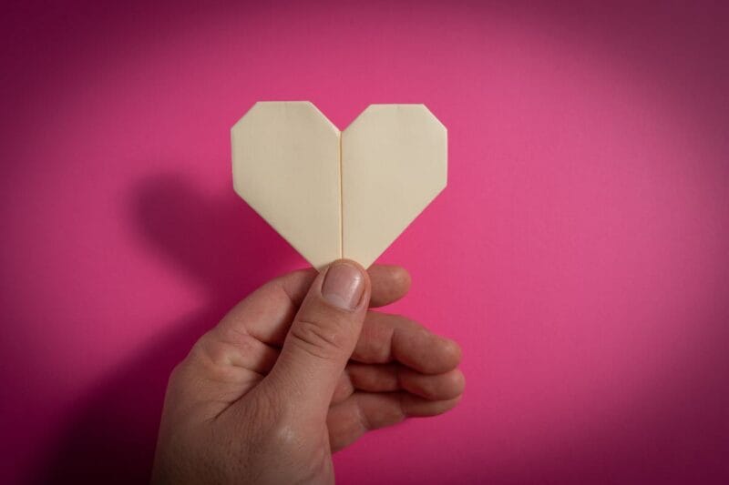 Eine Hand präsentiert ein Herz aus Papier, das mit der Technik Origami Herz falten hergestellt wurde.