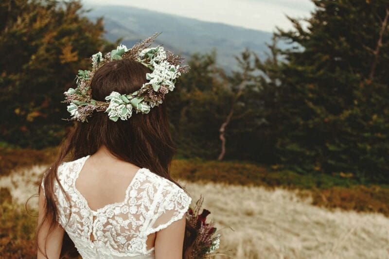 Die Rückansicht einer Braut, die ein Kleid mit Spitzenrücken trägt und einen Blumenkranz auf ihrem Haar hat. Weiße Hochzeit Bedeutung.