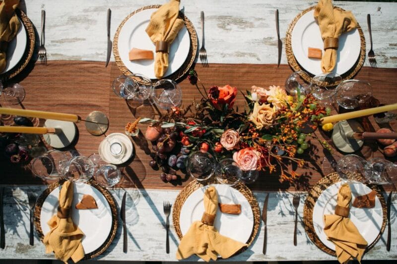 Stilvolle Tischdekoration für eine goldene Hochzeit im Freien mit natürlichen Blumenarrangements, rustikalen Holztischen und eleganten Servietten.