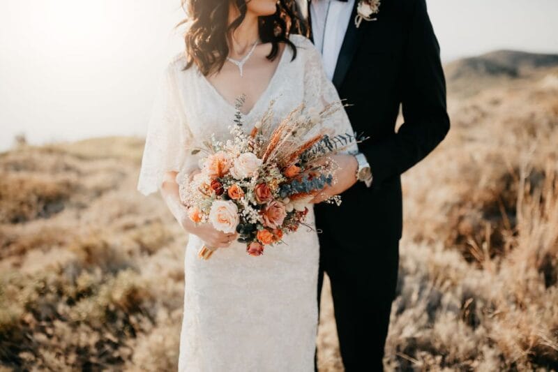 Brautpaar bei rustikaler Hochzeit im Freien mit schönem Blumenstrauß