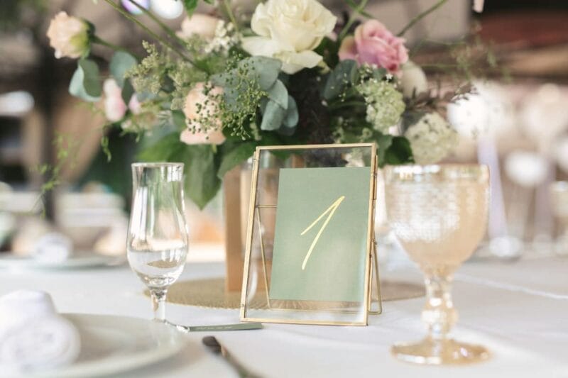 Boho-Stil Tischnummern Hochzeit mit zwei Gläsern und Blumenstrauß.